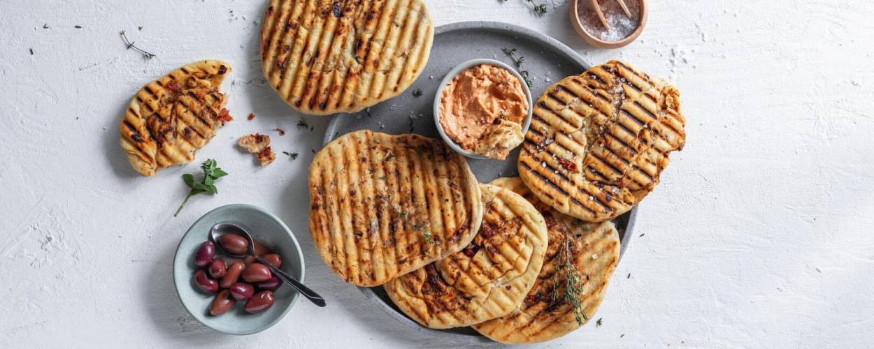 Grillbrot mit Oliven und Dip auf grauem Teller