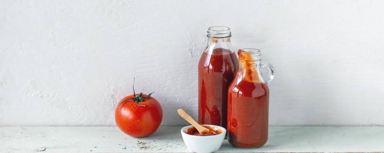 Rote Soße in Glasflaschen und Schälchen mit Tomate