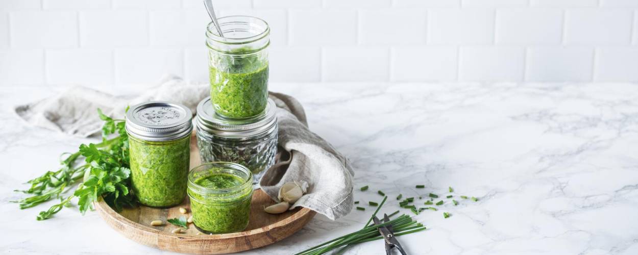 Grünes Pesto in drei Gläsern mit Petersilie und Schnittlauch auf Holzbrett