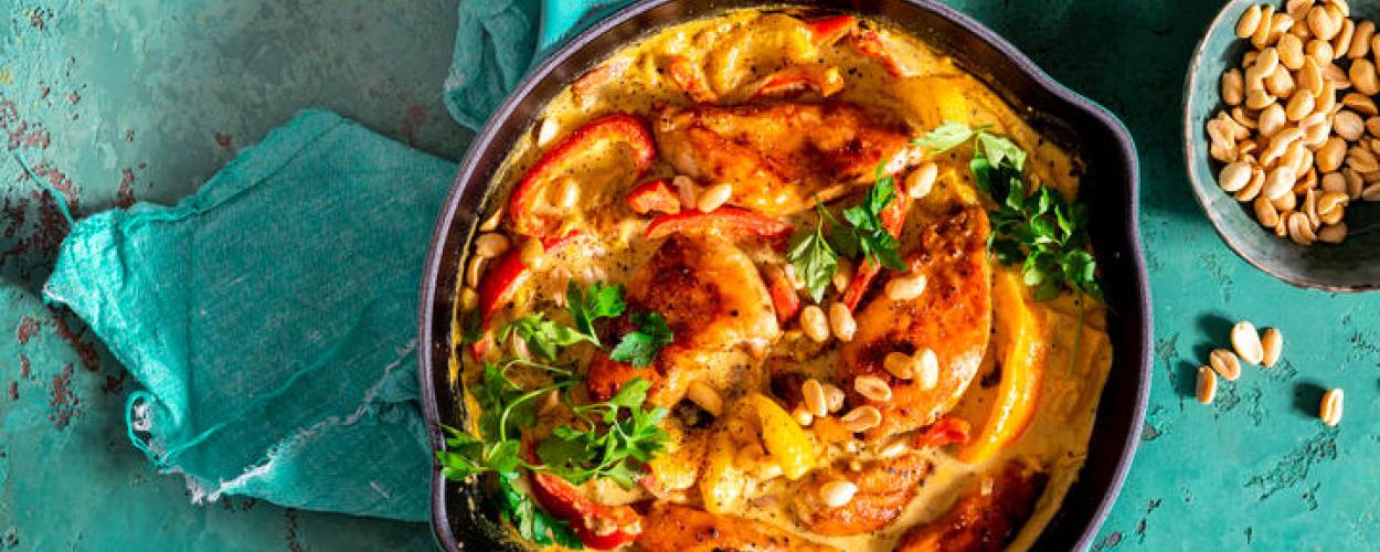 Hähnchencurry in türkisener Pfanne mit Reis und Erdnüssen in Schüsseln