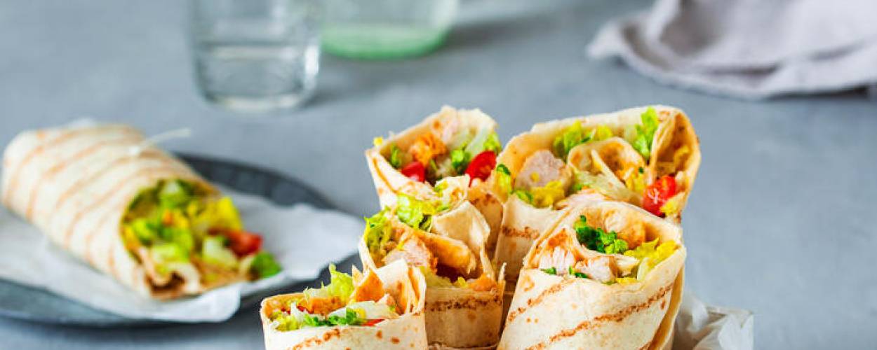 Wraps gefüllt mit Salat und Gemüse in weißer Box mit Dip in Schale