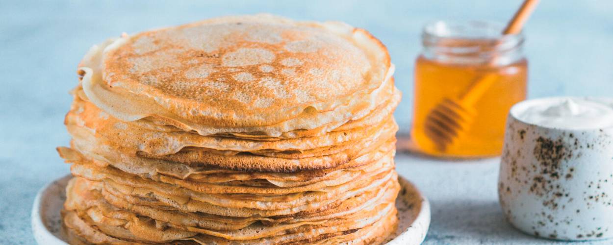 Pfannkuchen gestapelt auf weißem Teller mit Honig im Glas