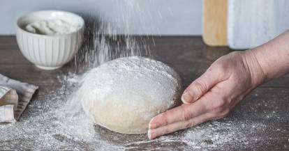 Mehl wird auf einen Brotteig gestreut.