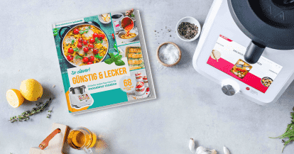 Neues ZauberMix-Kochbuch "Günstig & Lecker" liegen neben dem Monsieur Cuisine und umringt von Zutaten auf einer Arbeitsplatte