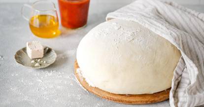 Pizzateig halb abgedeckt mit einem Küchentuch