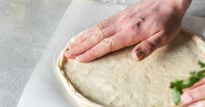 Pizzateig wird mit den Händen ausgerollt.