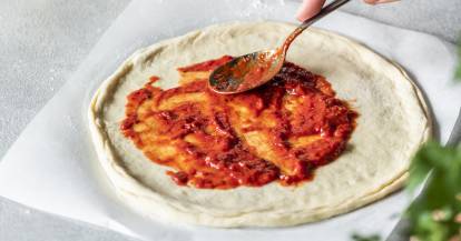 Ausgerollter Pizzateig wird mit Tomatensoße bestrichen.