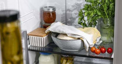 Abgedeckter Pizzateig in einem gefüllten Kühlschrank.