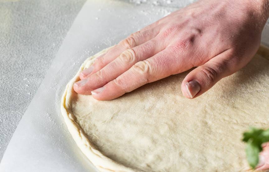 Pizzateig wird mit den Händen ausgerollt.