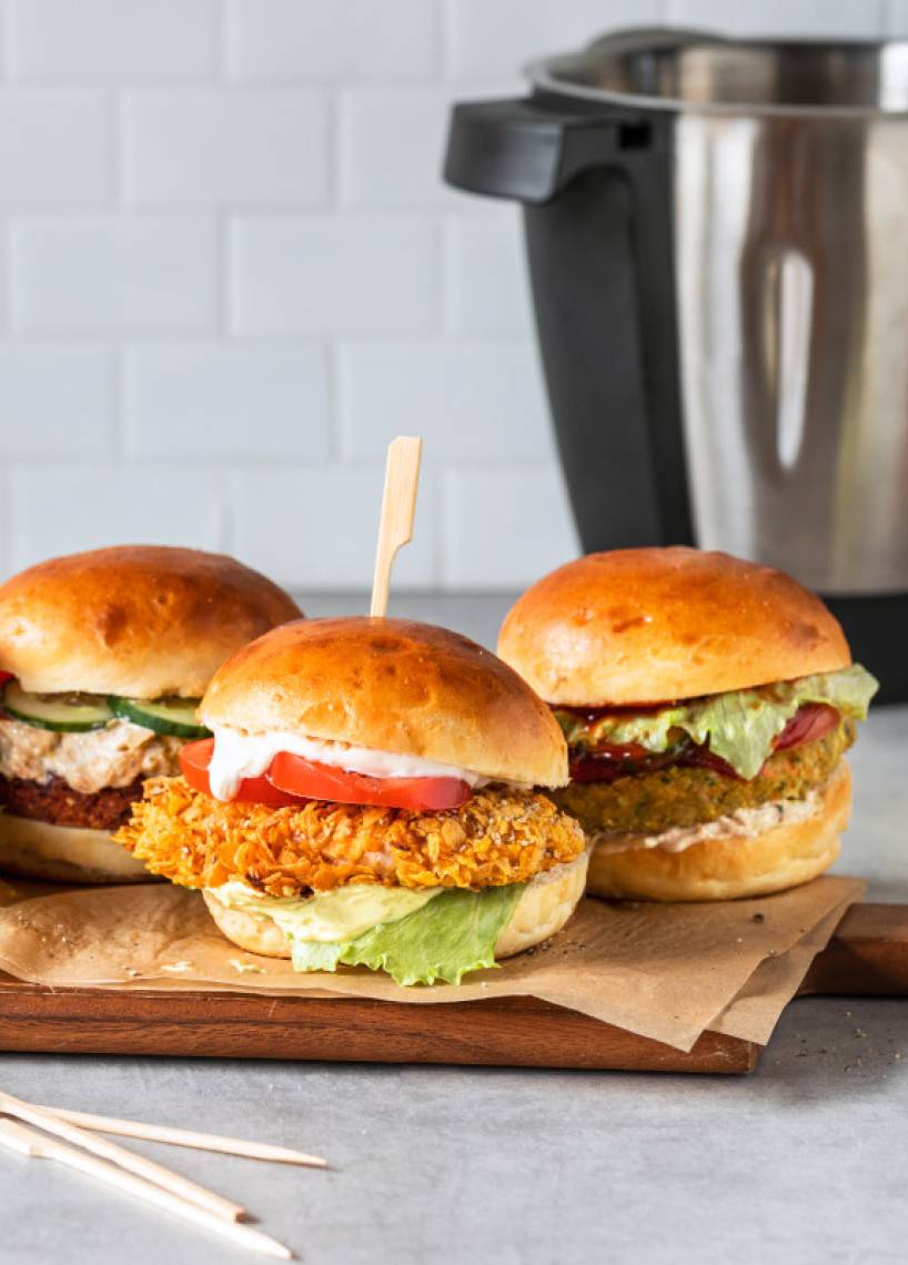 Vier Burger auf Holzbrett vor Mixbehälter Vier Burger auf Holzbrett vor Mixbehälter